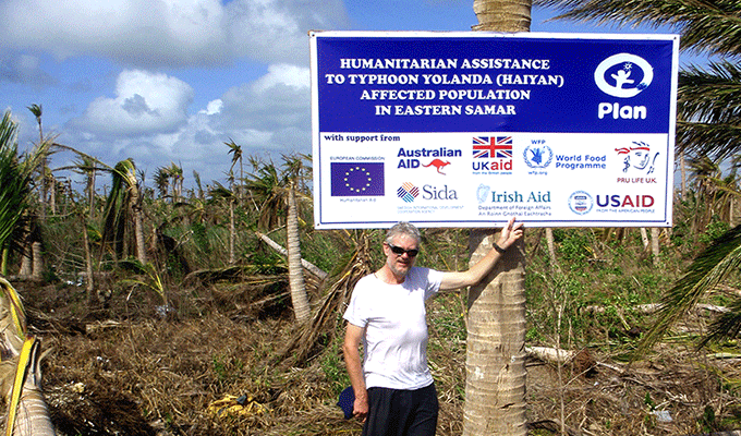 Michael Lee, Irish Aid Rapid Responder, stands beside a sign which outlines Irish Aid's support for the Typhoon Haiyan relief efforts among other donors. 
